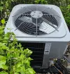 outdoor air conditioning unit surrounded by green bushes