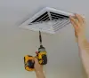 Person using a drill to remove an air vent from the ceiling.