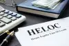 A HELOC document on a desk with a pen, calculator, notebook, and cash.