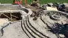 Stone patio and fire pit under construction with excavators and unfinished seating area.