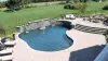 Curved backyard pool with stone waterfall, patio seating, and view of large grassy yard.