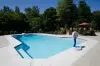 A backyard swimming pool with clear water, surrounded by trees and patio furniture.