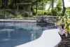 A curved pool with stone edging, flowers, and a small waterfall in a landscaped backyard.