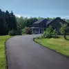 A newly-paved driveway in front of a blue farmhouse.