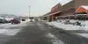 Snowy parking lot outside a Home Depot store with cars and slushy tire tracks on the ground.