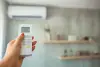 Hand holding remote control, setting temperature on air conditioner in a modern living room.