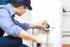 man in blue shirt turning a dial on a water heater