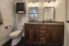 Modern bathroom with double sinks, wood cabinets, wall shelves, and black hexagonal floor tiles.