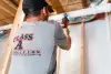 Man in a Class A Construction shirt uses a power drill on a white pipe in a basement.