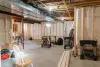 Unfinished basement with exposed beams, tools, plastic-covered walls, and scattered equipment.