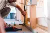Person installing electrical outlet box on wooden framing during house construction.
