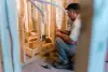 A man kneels while installing electrical wiring in a wooden-framed room under construction.