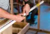 Person measuring and marking a white PVC pipe with a tape measure in a construction setting.