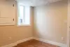 Small empty room with beige walls, wood flooring, a window, and a white door.