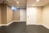 A finished basement room with beige walls, two white doors, and a small window.