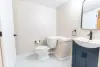 Minimalist bathroom with a toilet, small vanity, mirror, and white hexagon tile floor.