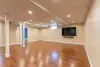 Spacious finished basement with wood flooring, beige walls, and a wall-mounted TV.