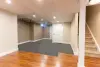 Finished basement with carpet, hardwood flooring, beige walls, white door, and carpeted stairs.