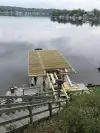 Three people work on building a dock by a calm lake, with houses visible in the background.