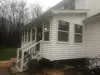 White house with enclosed porch, steps with railing, and trash can by the entrance on a cloudy day.