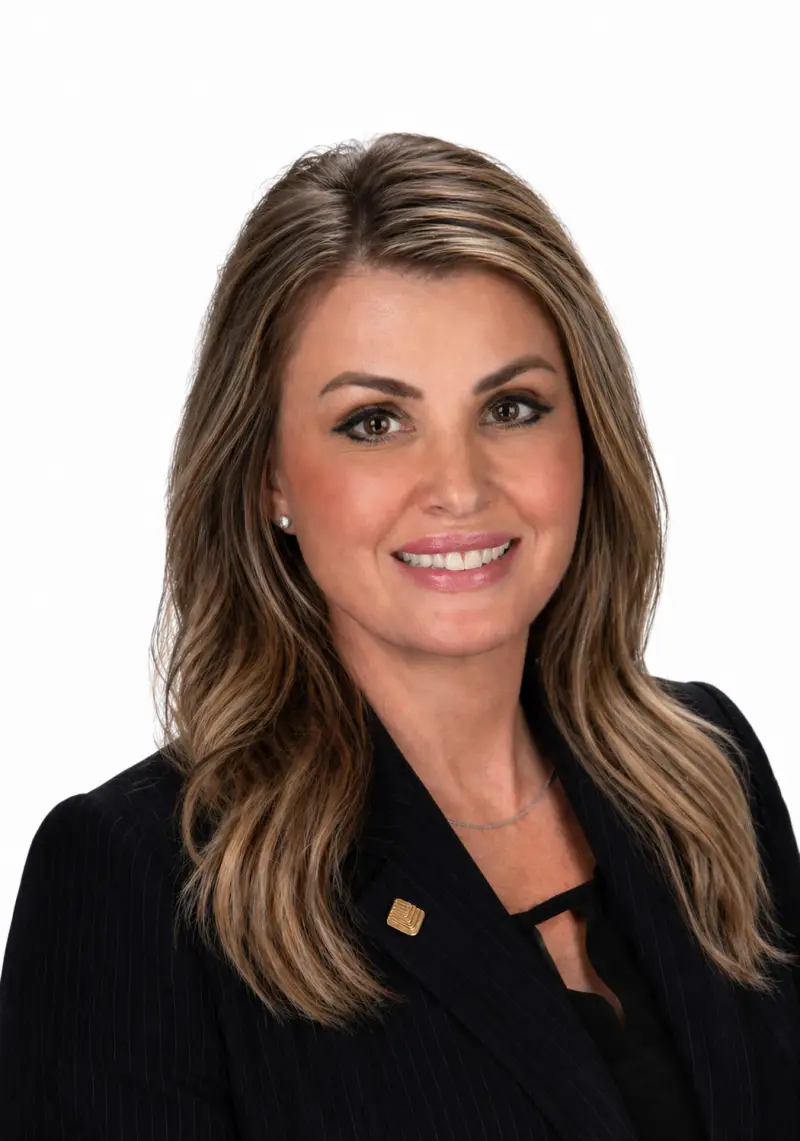 Smiling woman with long brown hair in a black blazer, posing for a professional headshot.